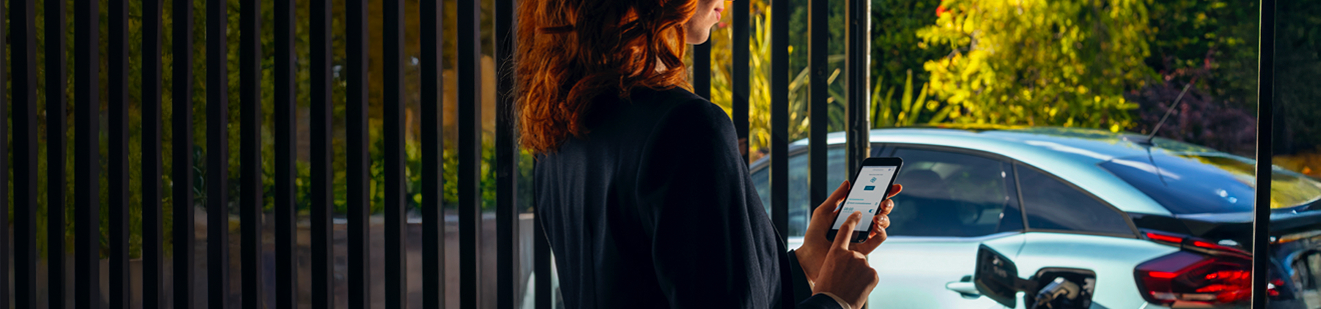 A lady looking at the My Leasys app on her mobile phone, there is a car in the background.