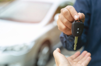 A person dressed in work overalls handing over a key to a customer.
