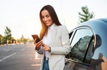 A woman looking at her mobile phone while leaning on a car.