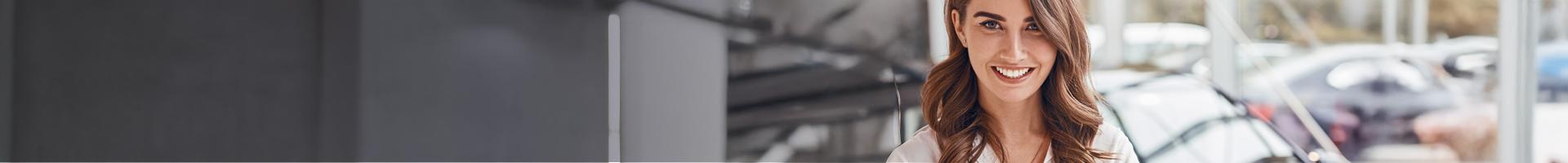 A woman standing in a car sales forecourt.