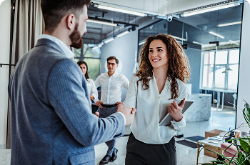 Two people dressed in office clothes shaking hands with another two people behind them.