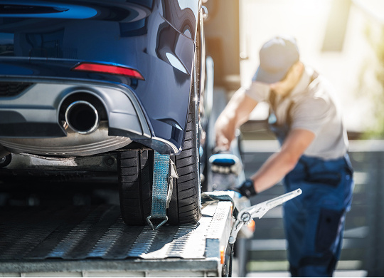 A man strapping a car onto a tow truck.