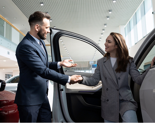 A woman getting in or out of a car and a man is shaking her hand.
