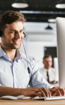 A man in a call centre with headphones on looking at a computer screen potentially serving a customer.