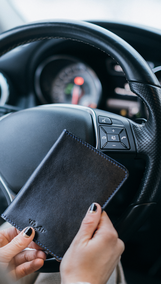 A person sat behind a steering wheel with only their hands present, clutching a wallet or card pouch.