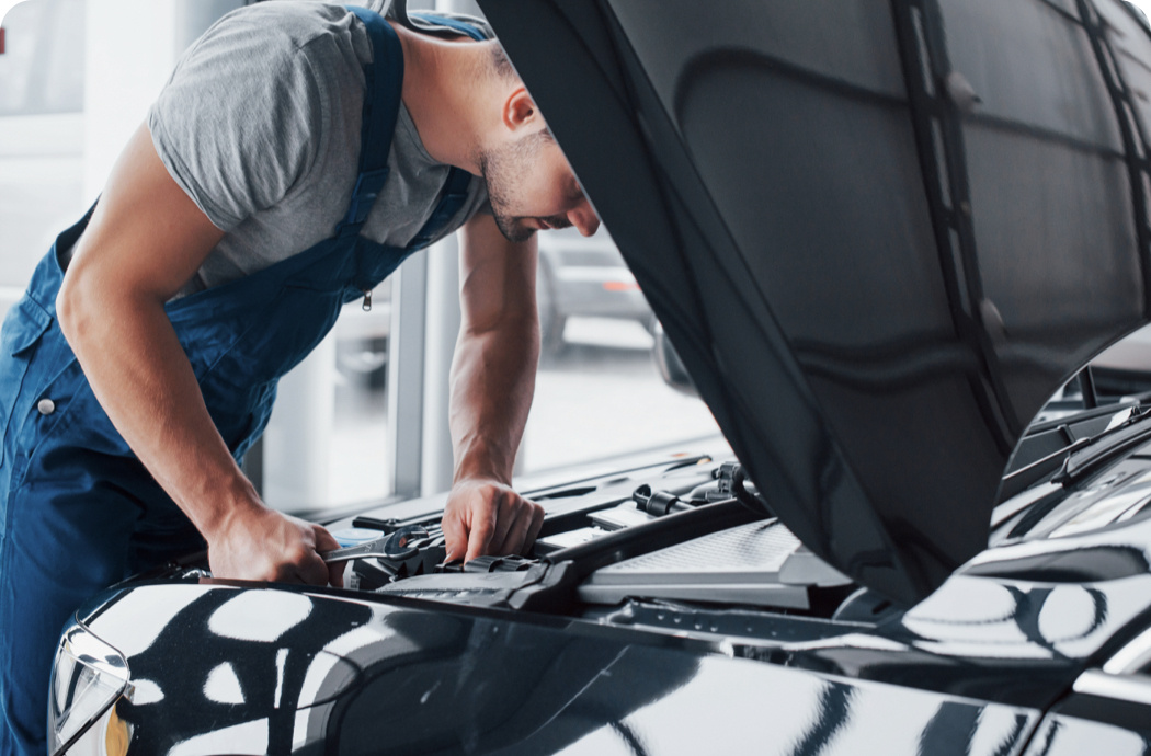 A man in overalls looking under the bonnet of a car.