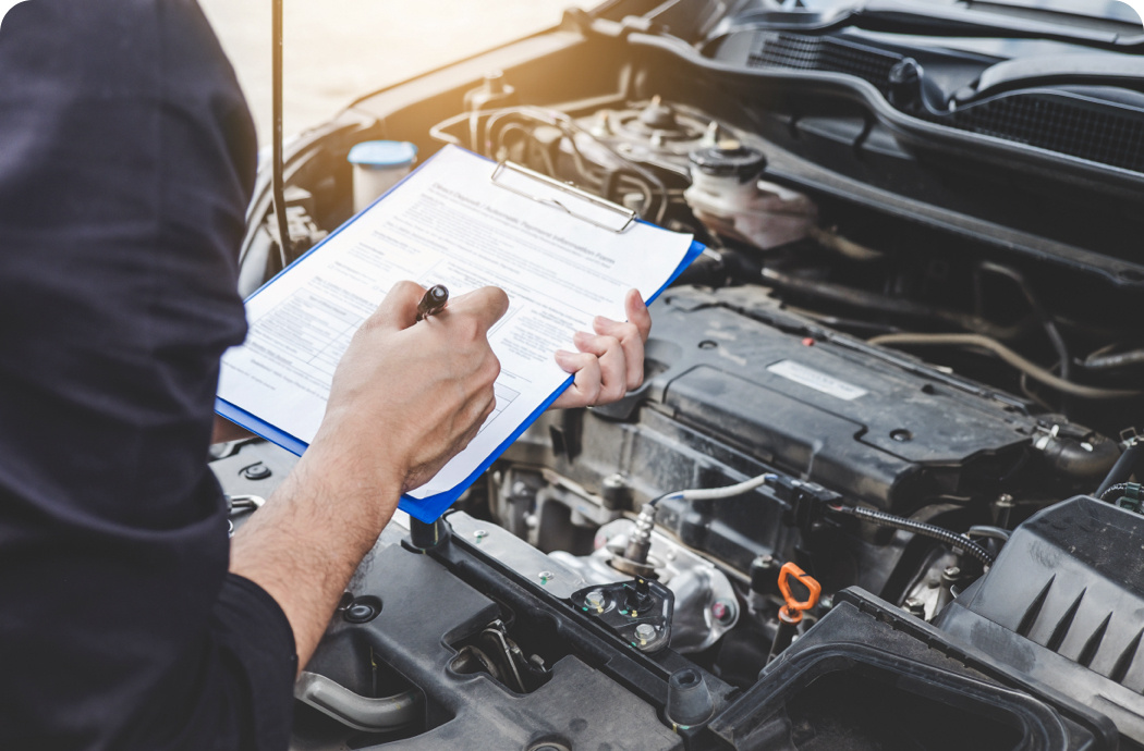 A person writing on a clipboard whilst looking under a bonnet of a car.