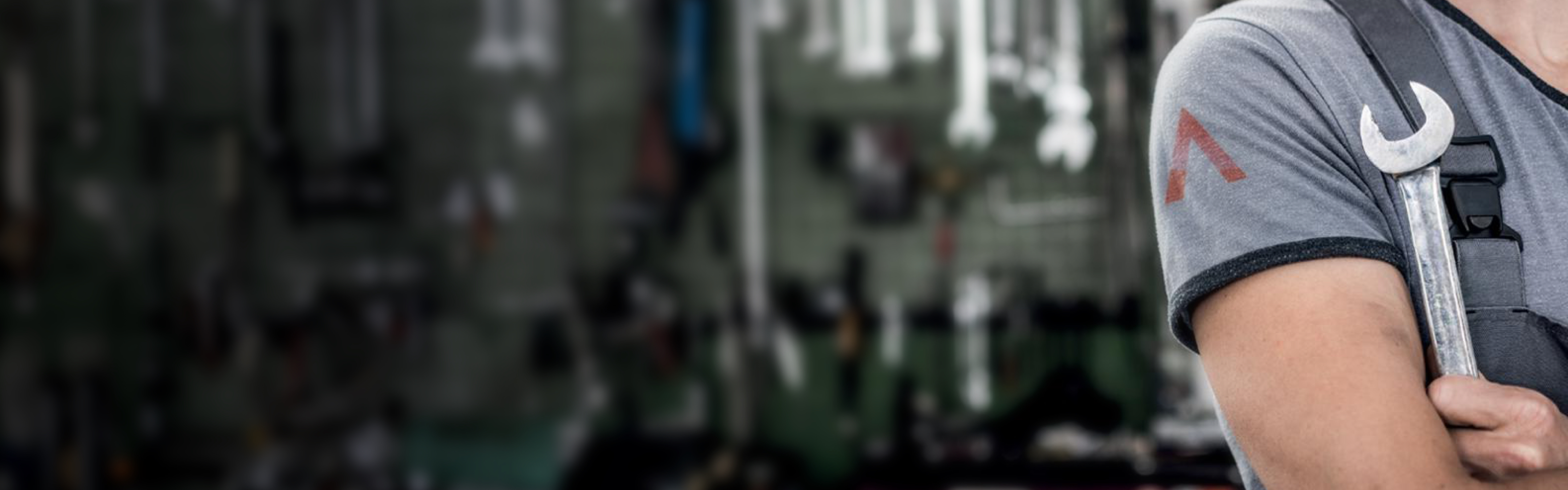 A picture of a person holding a spanner with spanners on the wall in the background