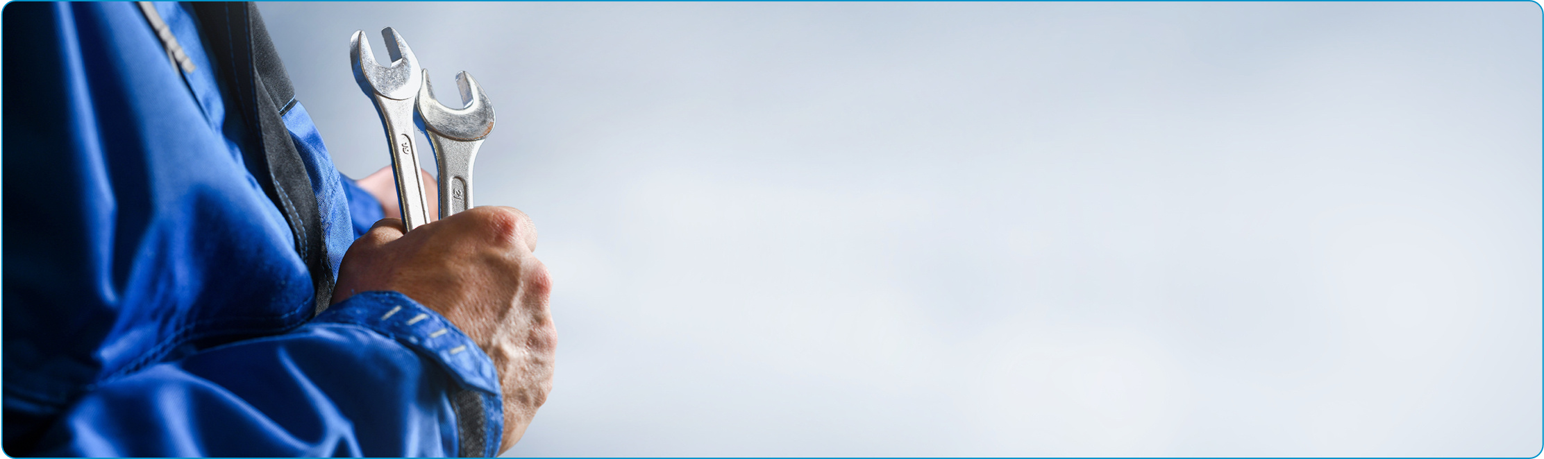 A person wearing blue overalls clutching two spanners.