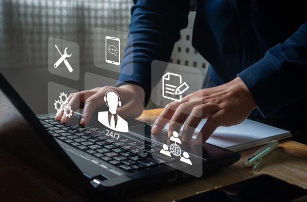 A man typing on a laptop surrounded with icons representing 24 hour support.