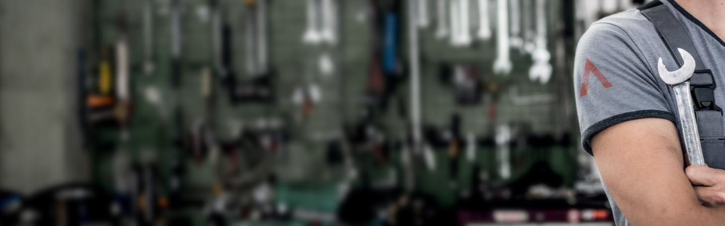 A man holding a spanner with more spanners behind him.