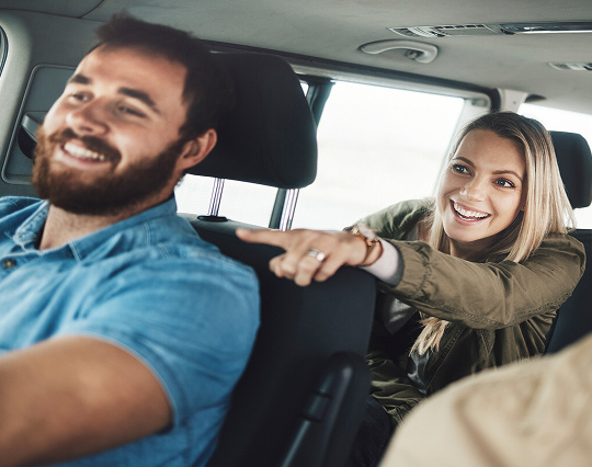 A man and a woman in a car, the man is driving.